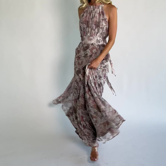 Model wearing the Tinsley Metallic Maxi Dress in Dusty Mauve featuring a high pleated halter neckline, defined waistband, tie-back keyhole detail, and a flowing chiffon maxi skirt with a dusty mauve floral print and subtle metallic shimmer.