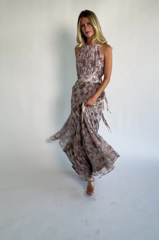 Model wearing the Tinsley Metallic Maxi Dress in Dusty Mauve featuring a high pleated halter neckline, defined waistband, tie-back keyhole detail, and a flowing chiffon maxi skirt with a dusty mauve floral print and subtle metallic shimmer.
