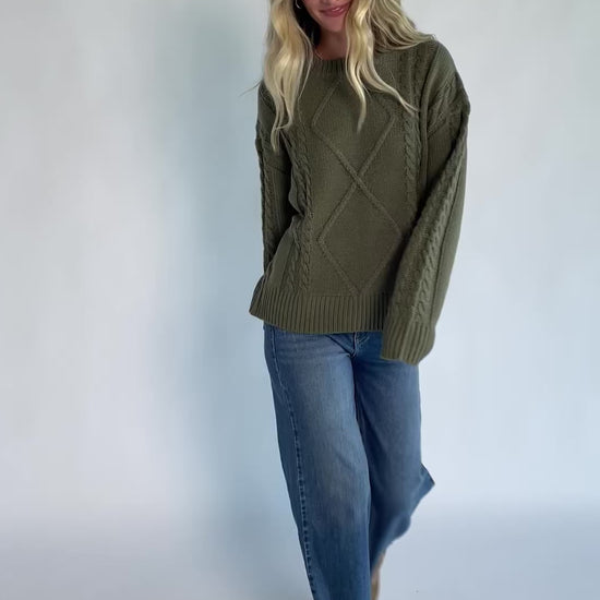 Model wearing an olive knit sweater with a round neckline, long drop-shoulder sleeves, and ribbed trim at the neckline, cuffs, and hem.