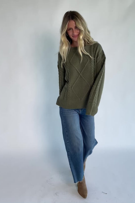 Model wearing an olive knit sweater with a round neckline, long drop-shoulder sleeves, and ribbed trim at the neckline, cuffs, and hem.
