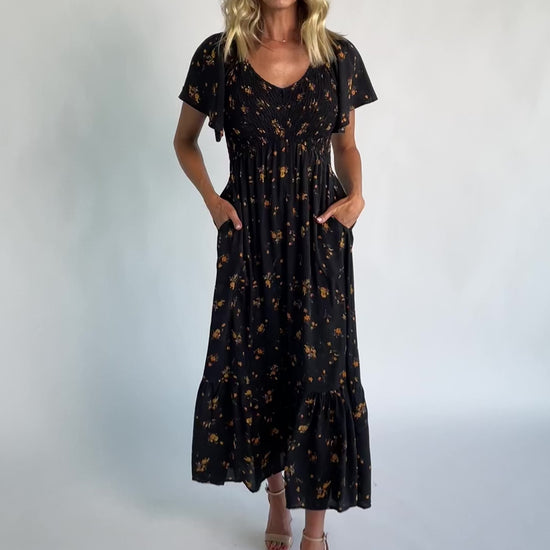 Model wearing a floral midi dress with a smocked bodice, wide V-neckline, and flutter sleeves.