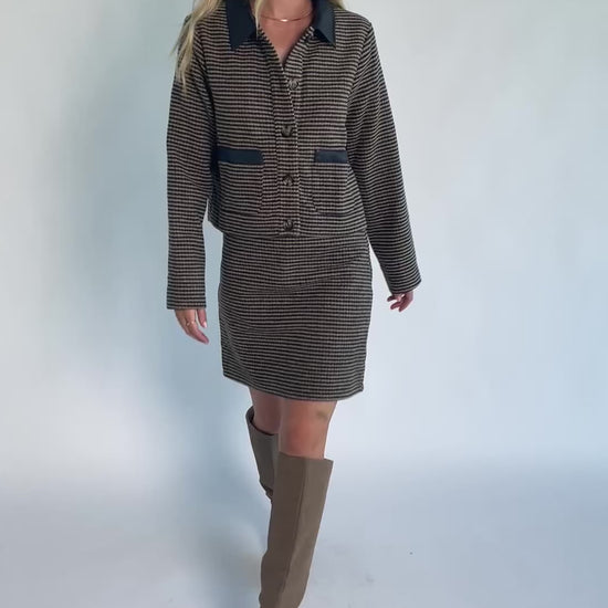 Model wearing the Gracey Set in Navy + Tan featuring a navy and tan striped tweed jacket with a collared neckline, faux leather trim, button-front closure, and matching mini skirt for a polished, coordinated look.