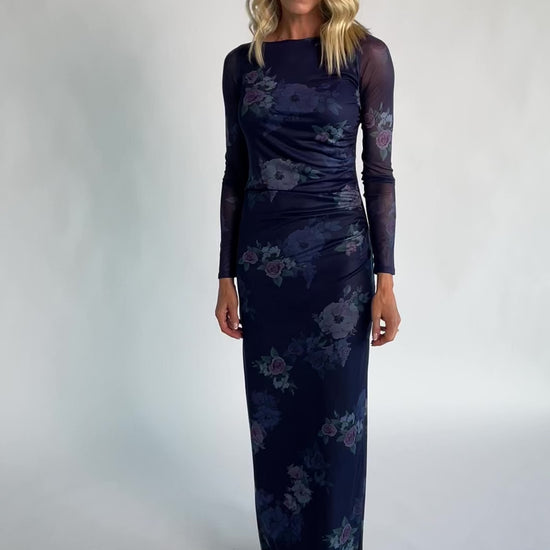 Model wearing a deep plum floral maxi dress with a fitted bodycon silhouette, sheer long sleeves, and a round neckline.