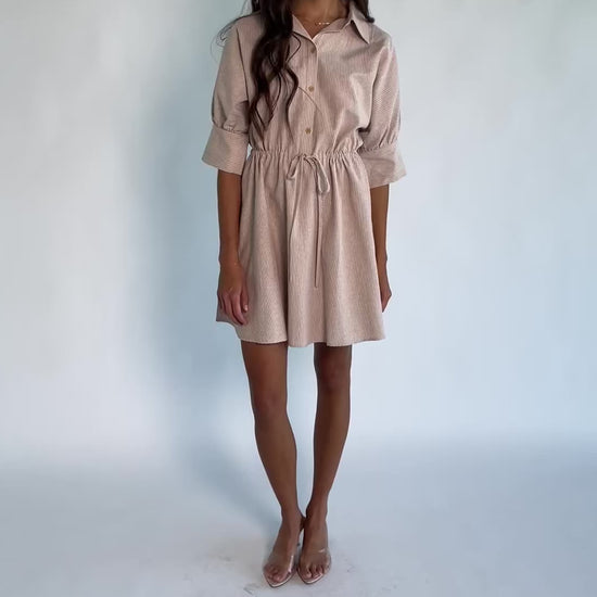 Model wearing the Beekman Short Dress in Natural Stripe featuring a collared neckline, functional button-front closure, elbow-length sleeves with wide cuffs, and a removable waist tie.
