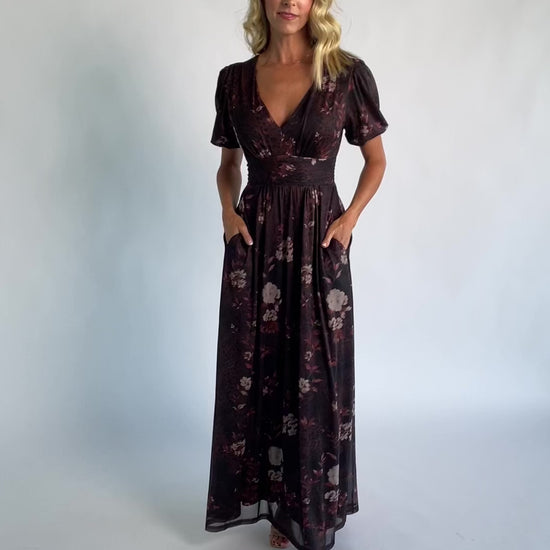 Model wearing a clove floral maxi dress with a deep V-neckline, short sleeves, and an empire waist.