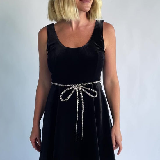 Julieta Short Dress in Black with a velvet finish, scoop neckline, and a rhinestone bow at the front waist.