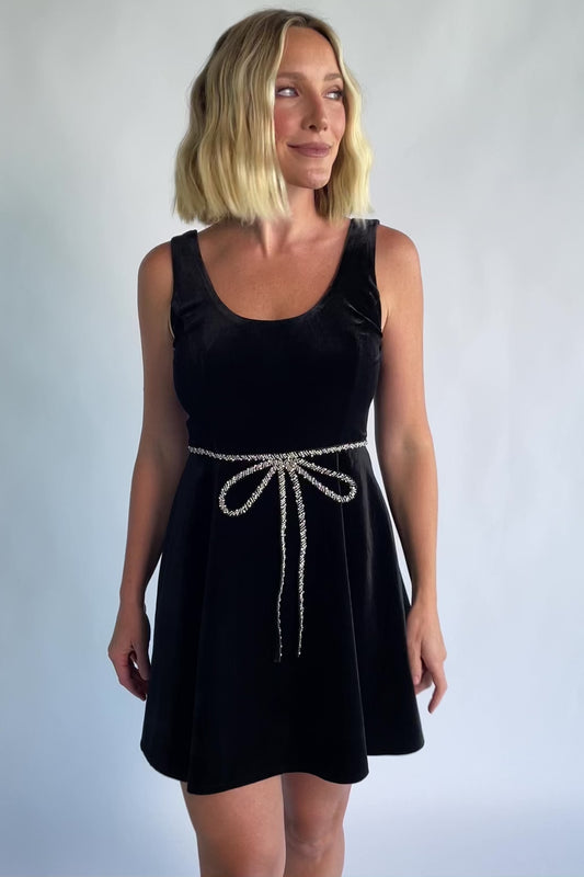 Julieta Short Dress in Black with a velvet finish, scoop neckline, and a rhinestone bow at the front waist.