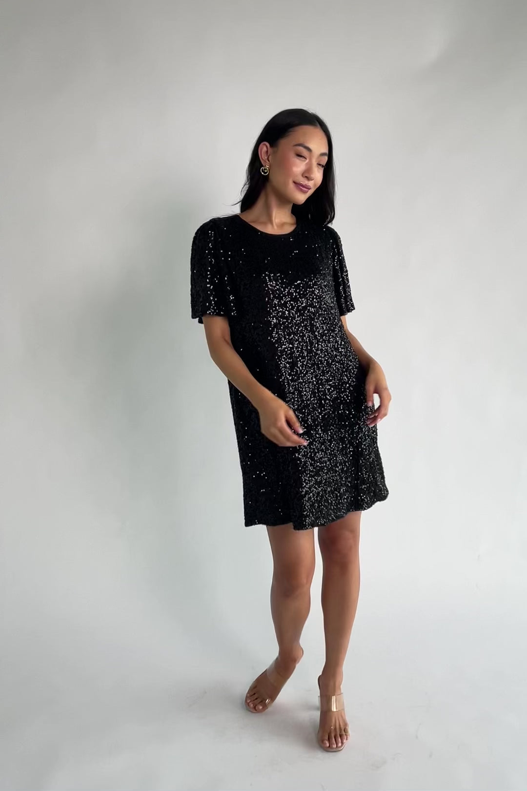 Black liquid sequin mini shift dress with a round neckline, short flutter sleeves, and a satin bow back detail.