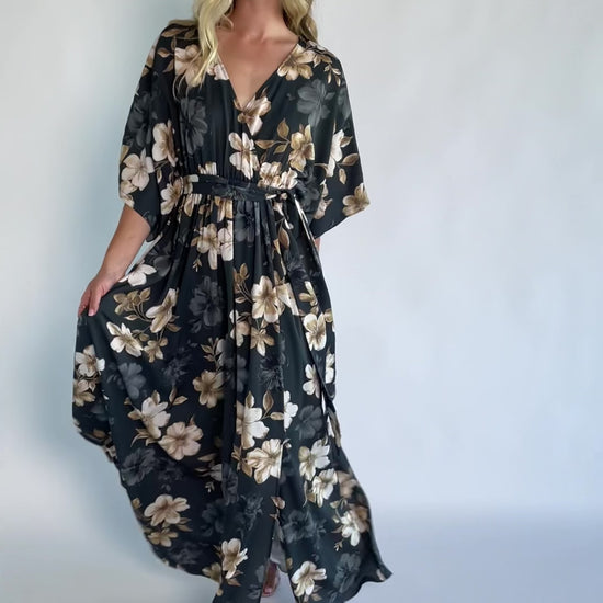 Model wearing a dark jade floral maxi dress with a surplice V-neckline, kimono sleeves, and an elastic waist with a removable sash tie.