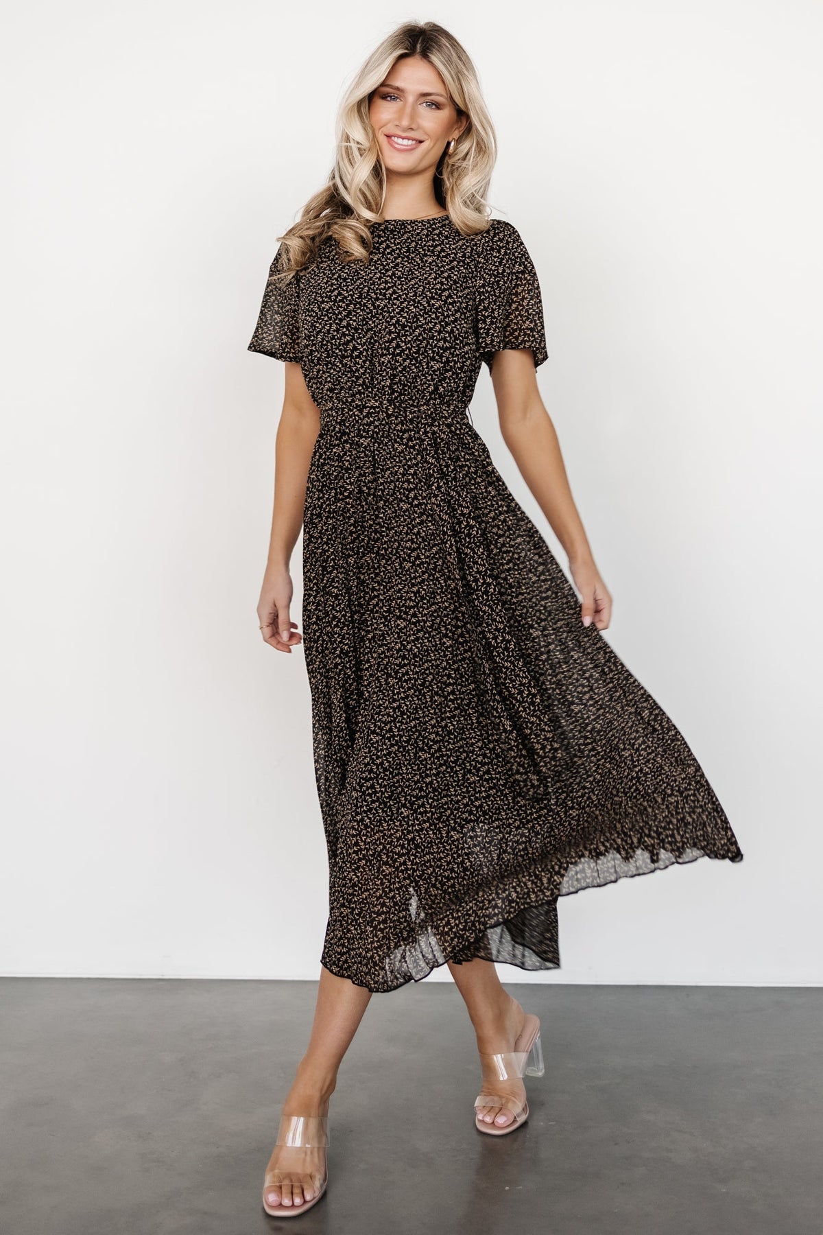 Side profile of the Prim Pleated Midi Dress highlighting the elastic gathered waist, removable self-tie, and flowing pleated skirt in floral print.