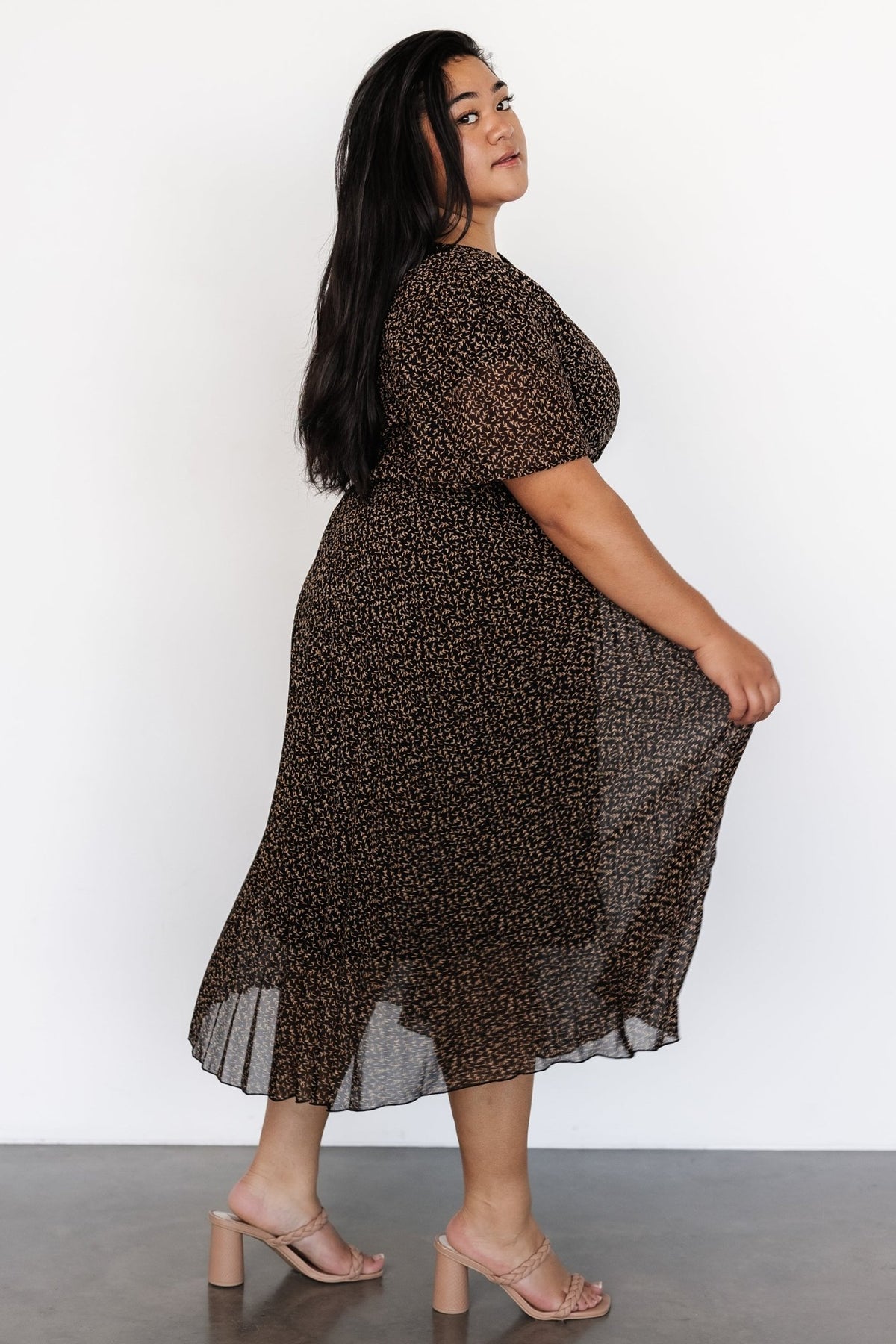 Styled look of the Prim Pleated Midi Dress worn with minimal accessories to showcase pleated movement and modest midi length in black print.