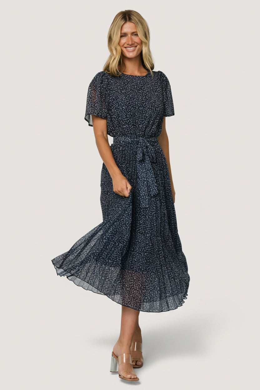 Front view of model wearing Prim Pleated Midi Dress in navy leaf print, chiffon bodice with round neckline and pleated midi skirt, removable tie.