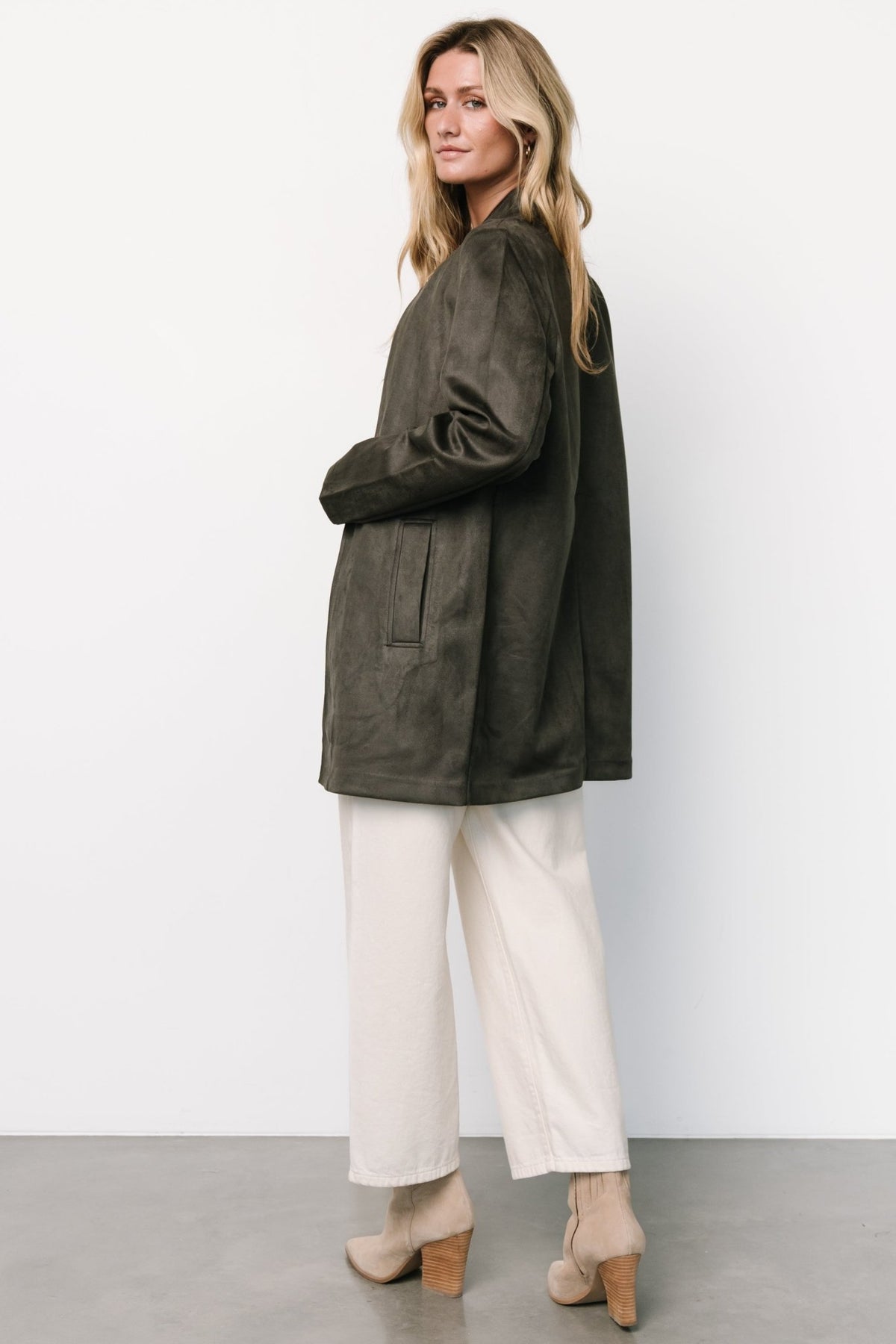 Model styling shot: jacket layered over dress with hands in functional pockets for a casual yet refined look.