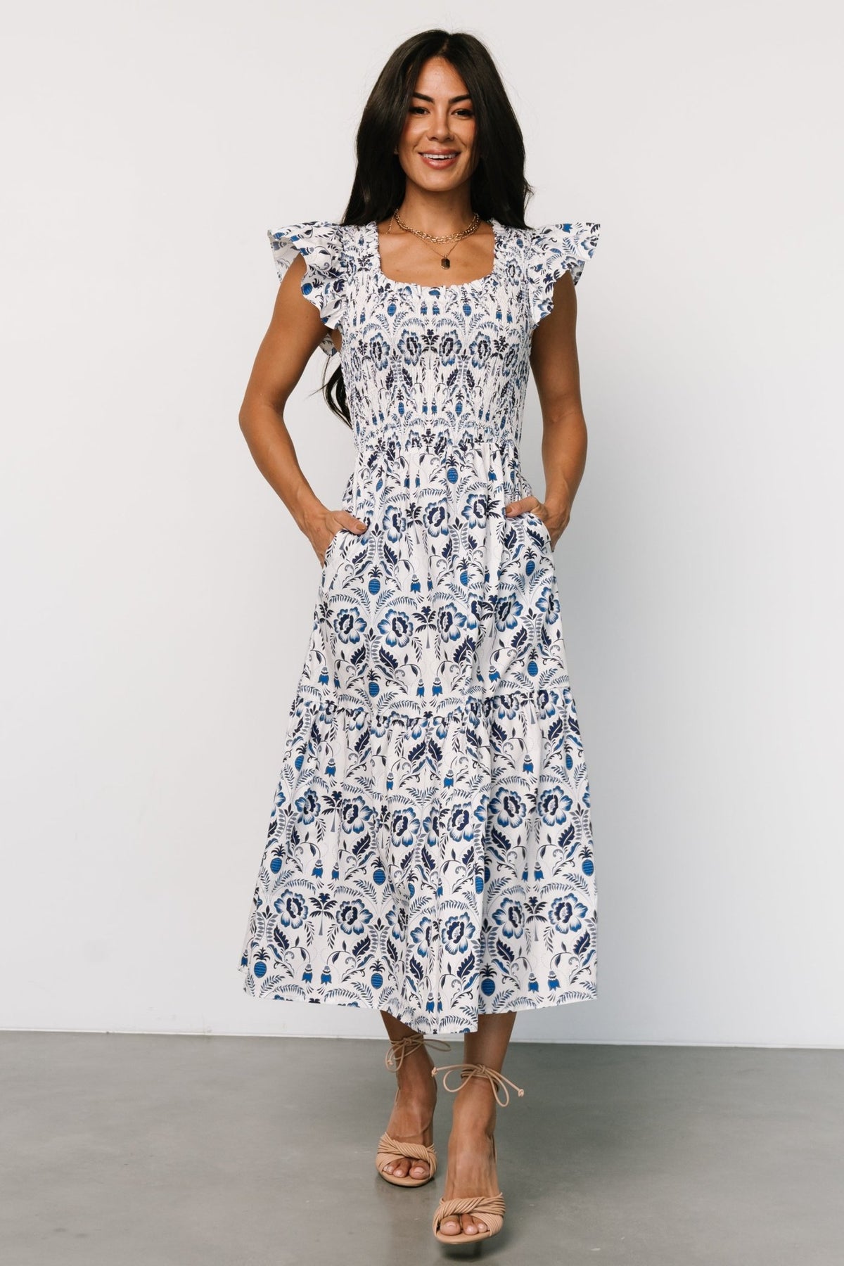 Front view of white midi dress with multi-shade blue floral print, smocked bodice, ruffled scoop neckline, and short flutter sleeves.