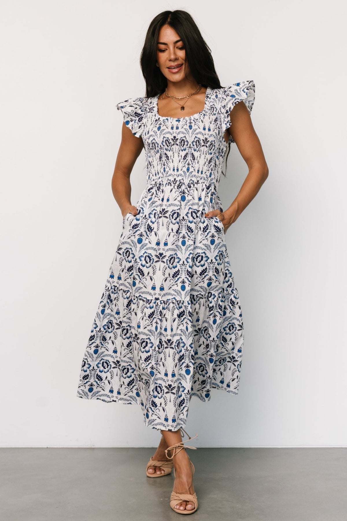 Back view of the white and blue floral midi dress highlighting the smocked back, skirt drape, and flutter sleeve silhouette.