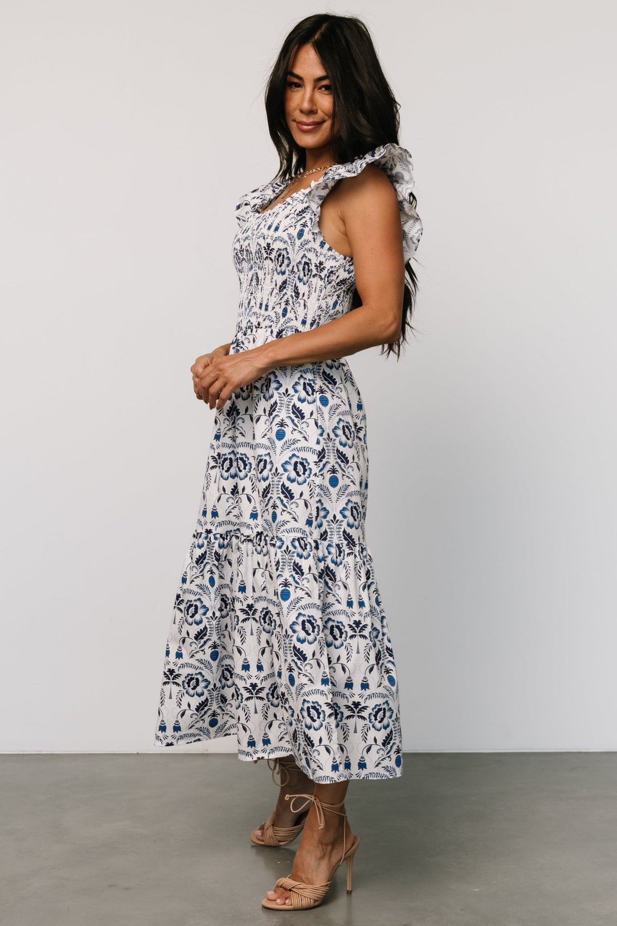 Close-up of smocked bodice and ruffled scoop neckline on a white dress with detailed multi-shade blue floral motifs and stitching.