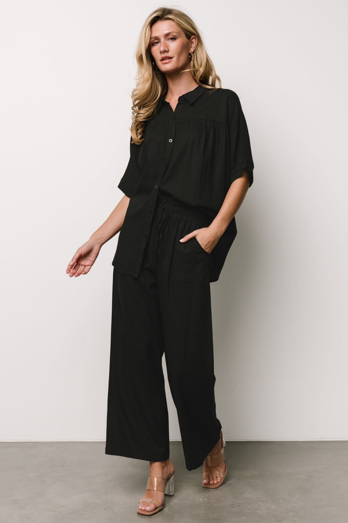 Model wearing black Romy Button Top with V-neck and dolman sleeves, styled for a casual yet polished look.