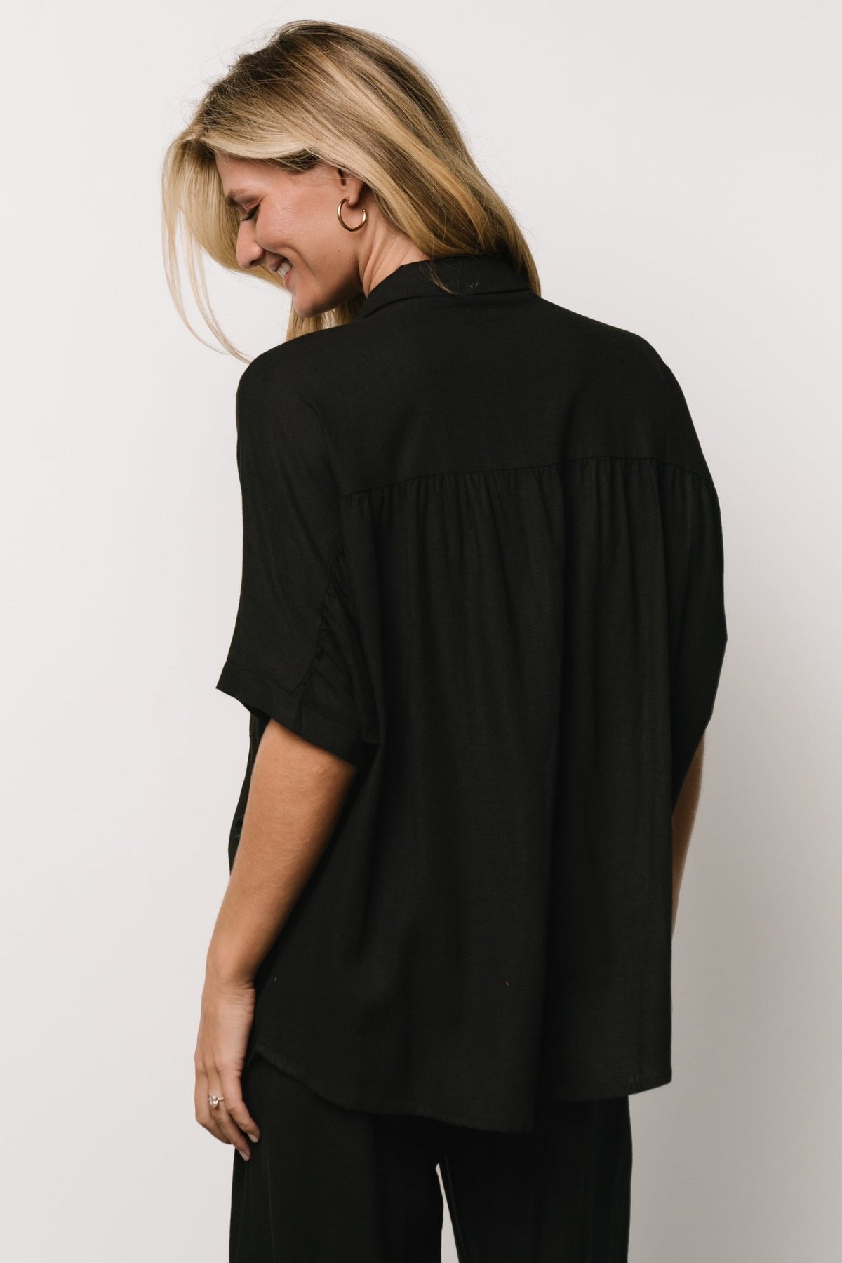 Flat-lay of the Romy Button Top in black beside matching Romy Pants, showing a coordinated travel-friendly outfit.