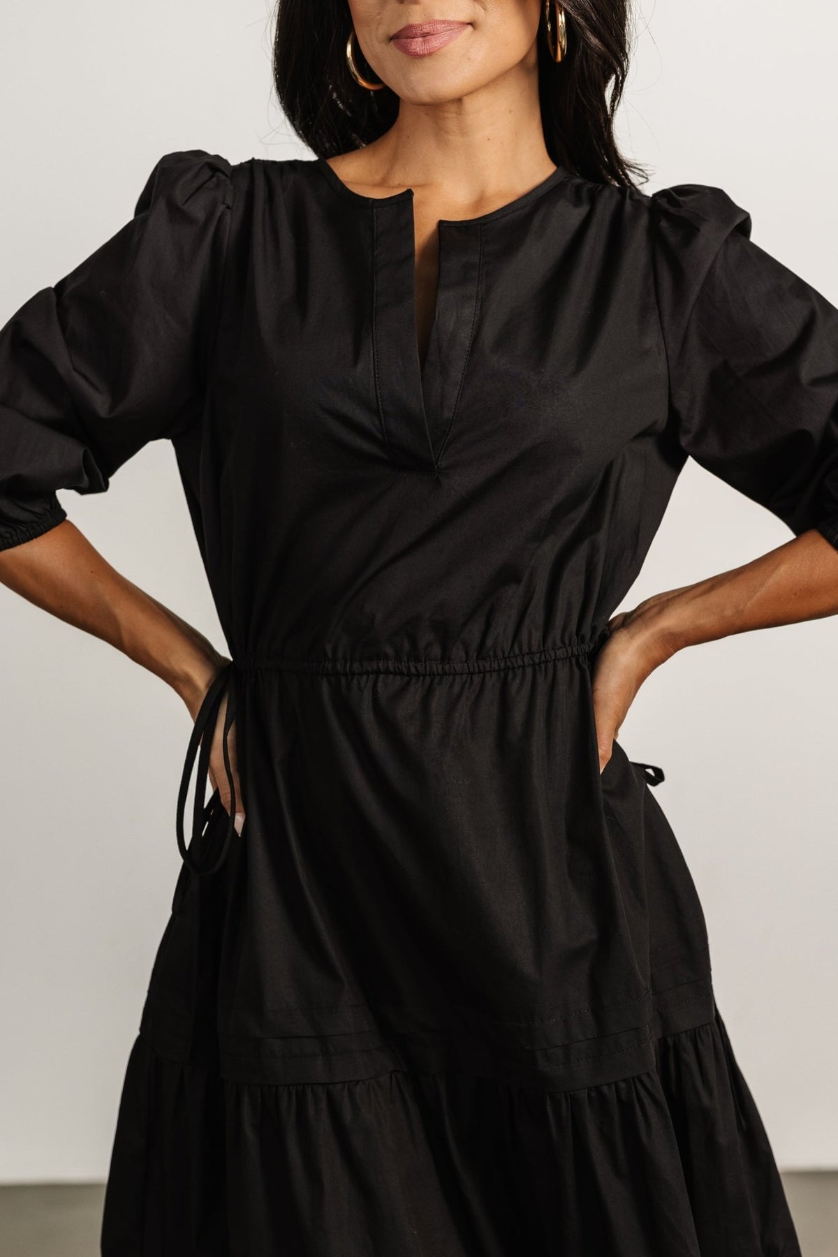 Model wearing the Santa Fe Poplin Midi Dress in black; highlights 3/4 sleeves with elastic cuffs, adjustable tie waist and flowing tiered hem for movement.