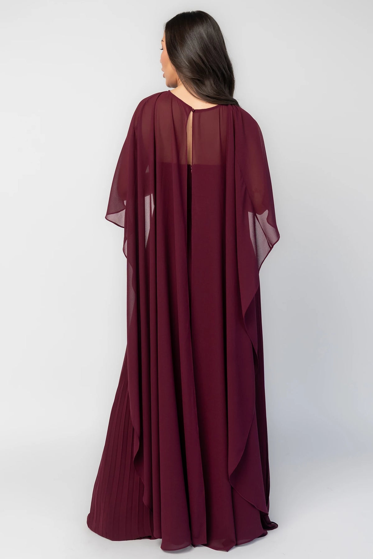 Serafina Strapless Gown in Burgundy with strapless neckline, removable sheer cape overlay, defined waist, and pleated skirt.