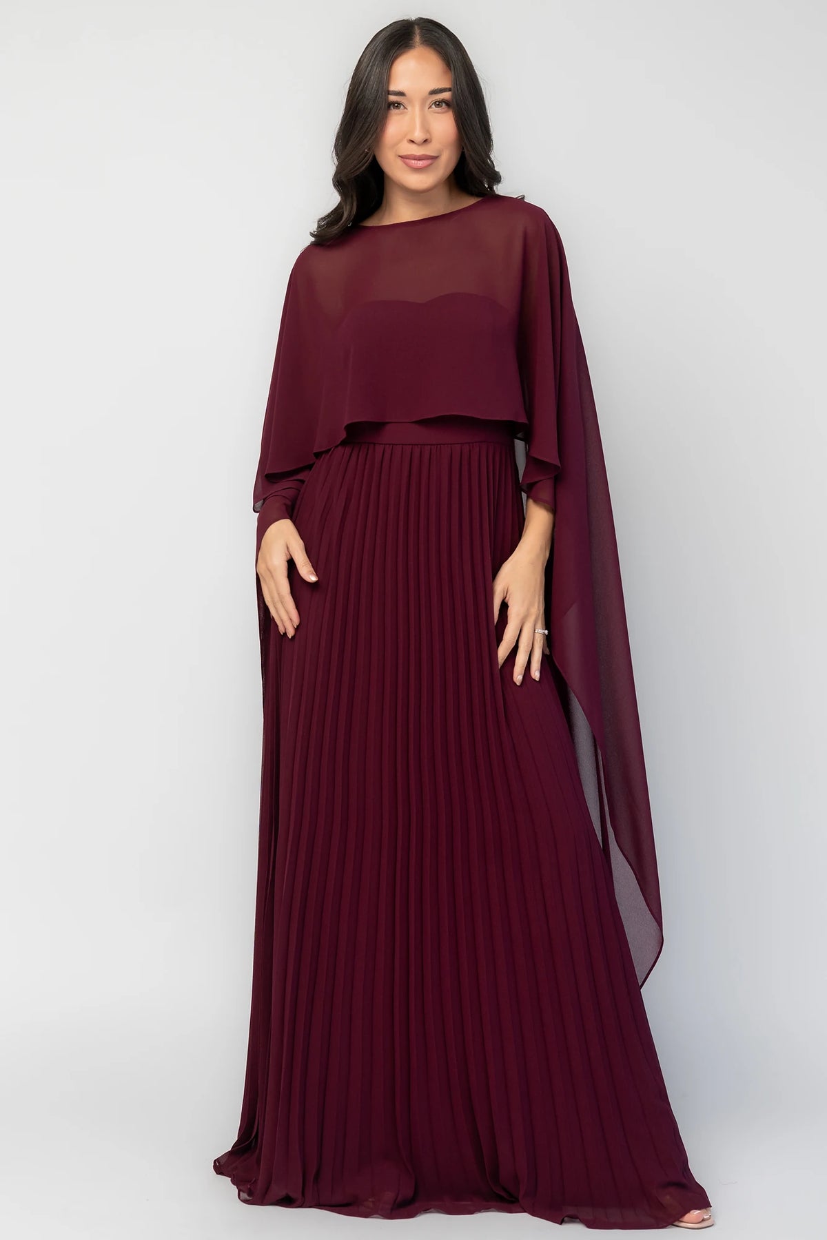 Serafina Strapless Gown in Burgundy with strapless neckline, removable sheer cape overlay, defined waist, and pleated skirt.