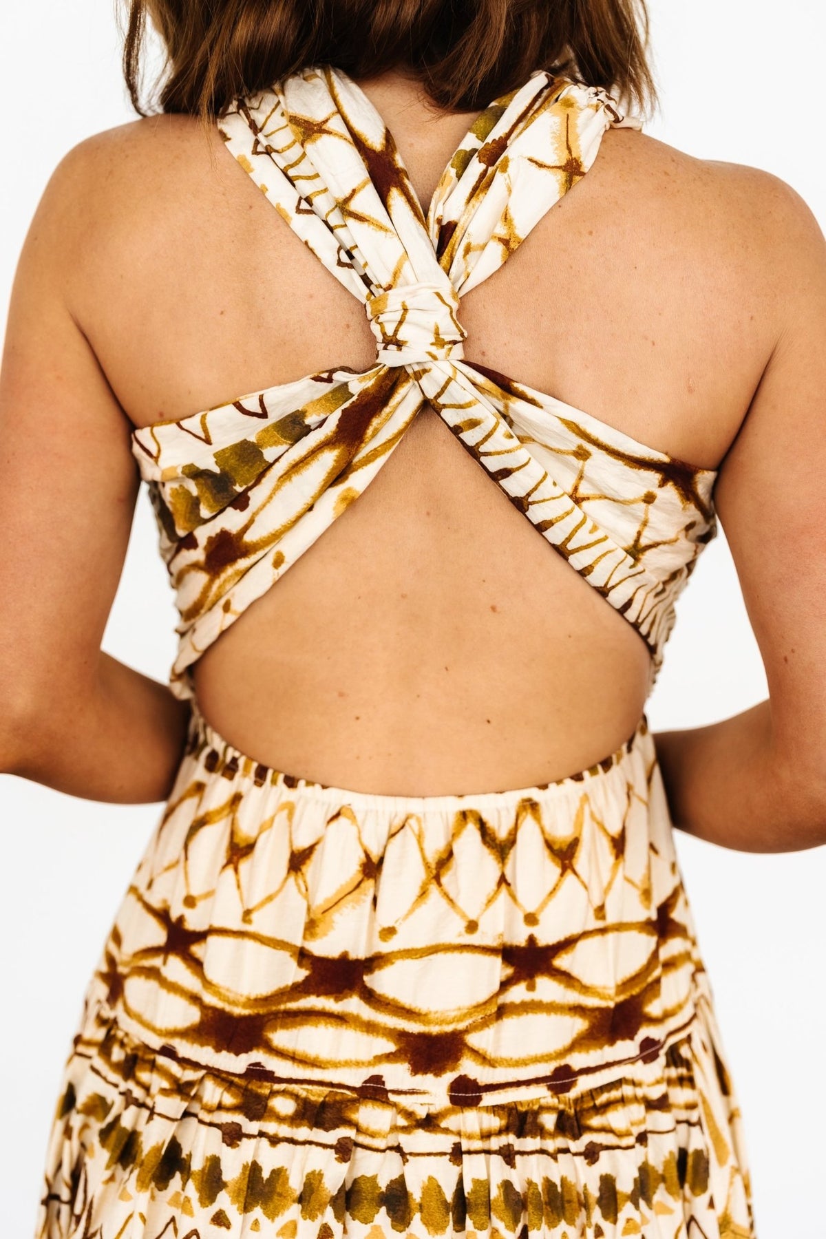Full-length view of tan multi printed midi dress hanging naturally to show cut, length, and tiered skirt detail.