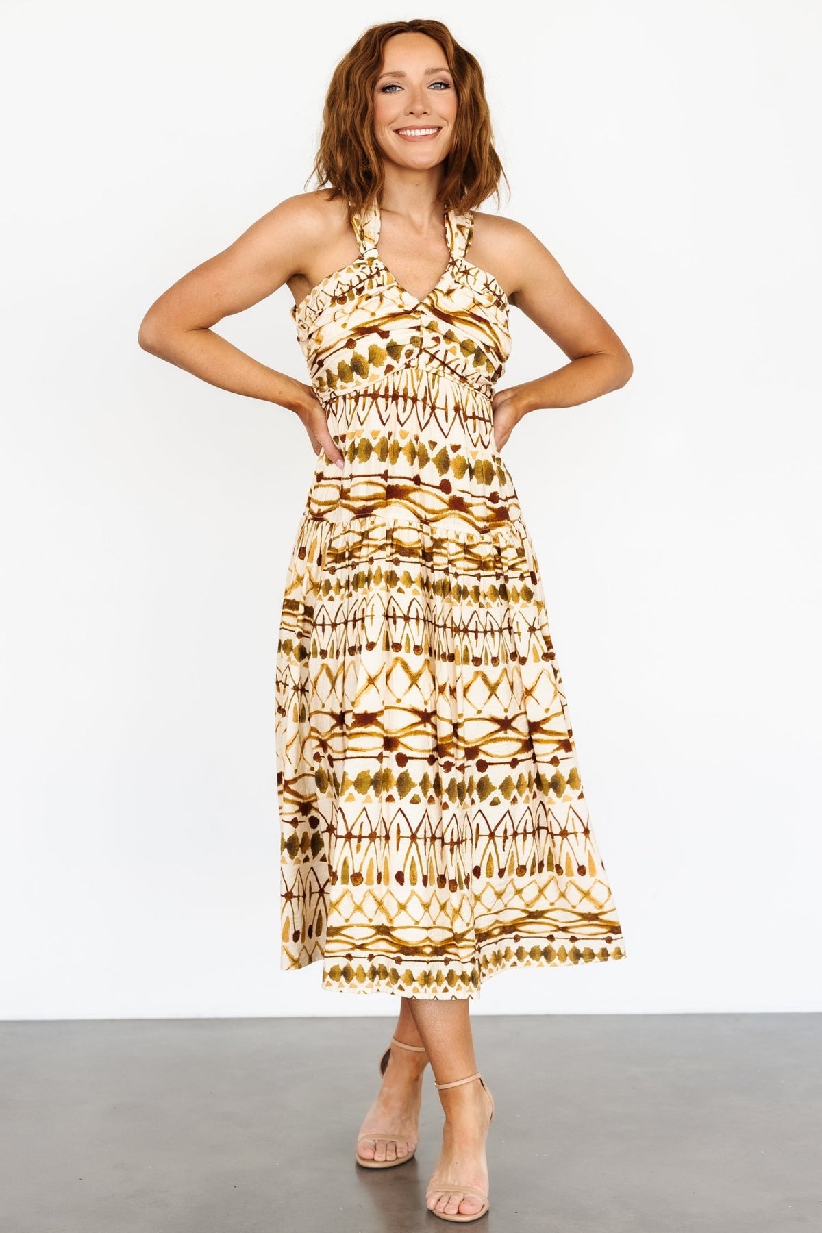 Front view of tan multi printed midi dress showing thick V-neckline, gathered bust, empire waist and single-tier skirt on model.
