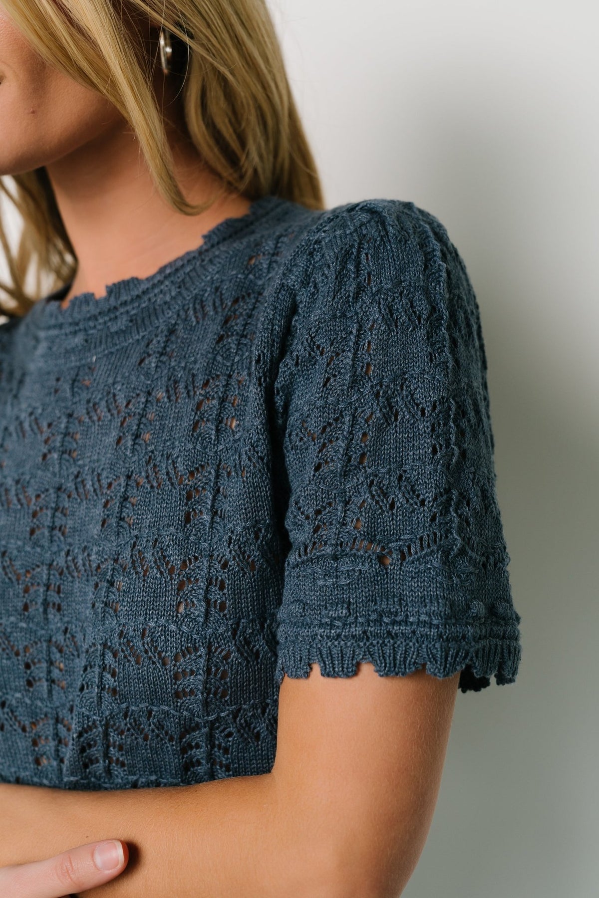 Studio image of Serenity crochet knit sweater top in slate blue styled with denim, showing length, scalloped trim, and overall fit.