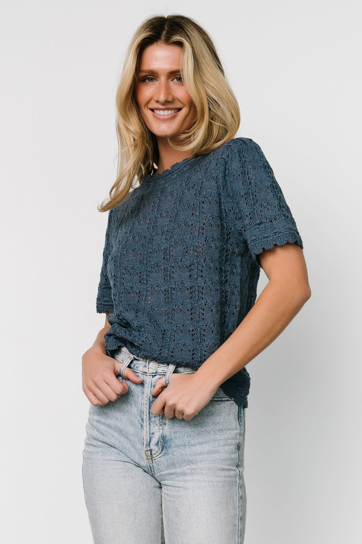 Front view of Serenity crochet knit sweater top in slate blue showing high neckline, short sleeves, scalloped collar, and open knit texture.