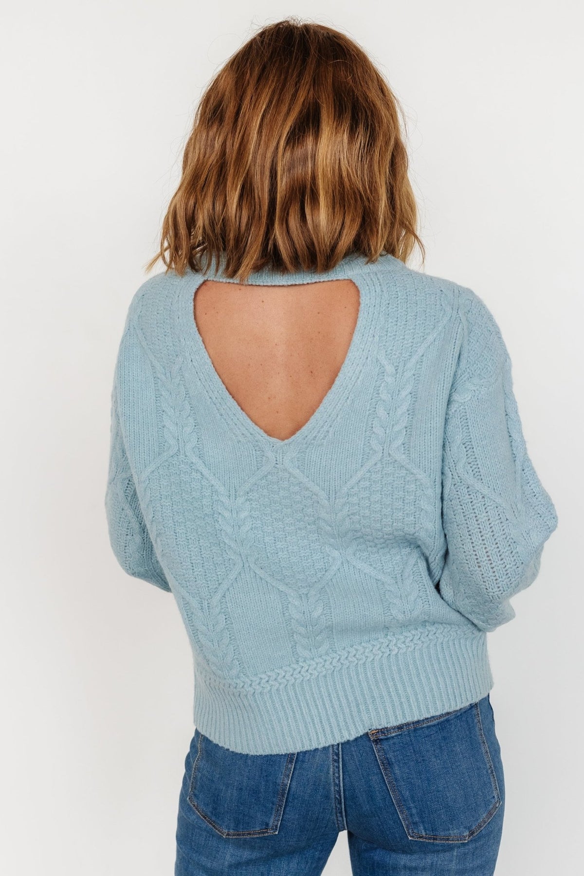 Styled flat-lay of Sheffield cable-knit sweater in light blue showing overall silhouette, round neckline, and textured knit pattern.