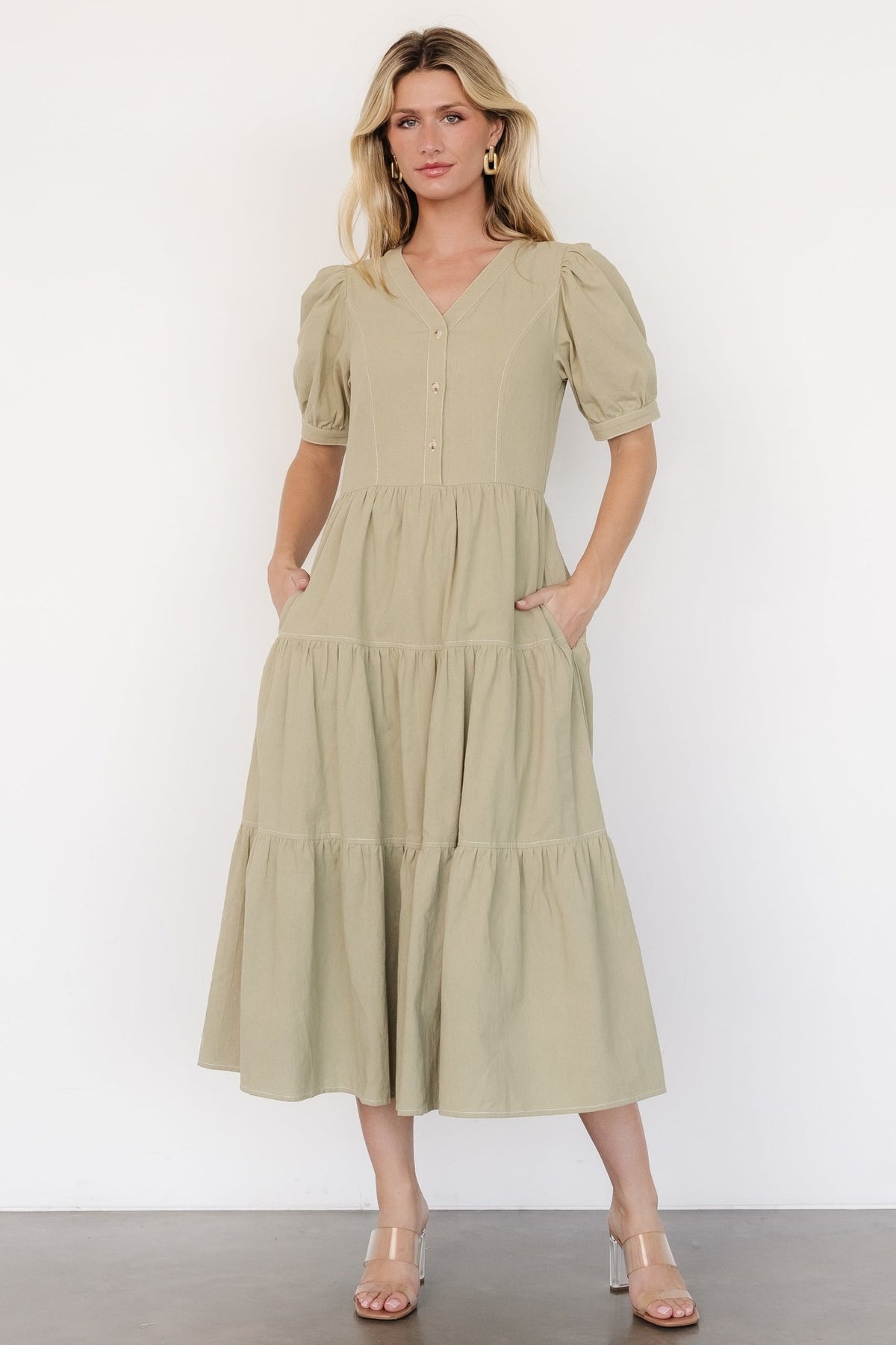 Front view of a sage green button-front midi dress with V-neck, puff sleeves, tiered skirt, elastic back waist, and side pockets.