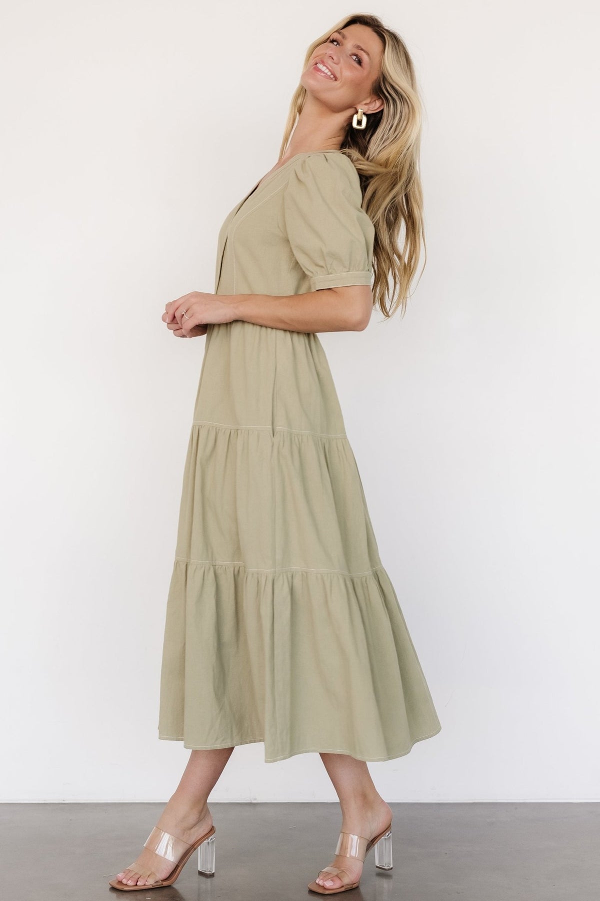 Close-up of puff sleeve with keyhole and single button on a sage green linen-look dress highlighting fabric texture and stitching detail.