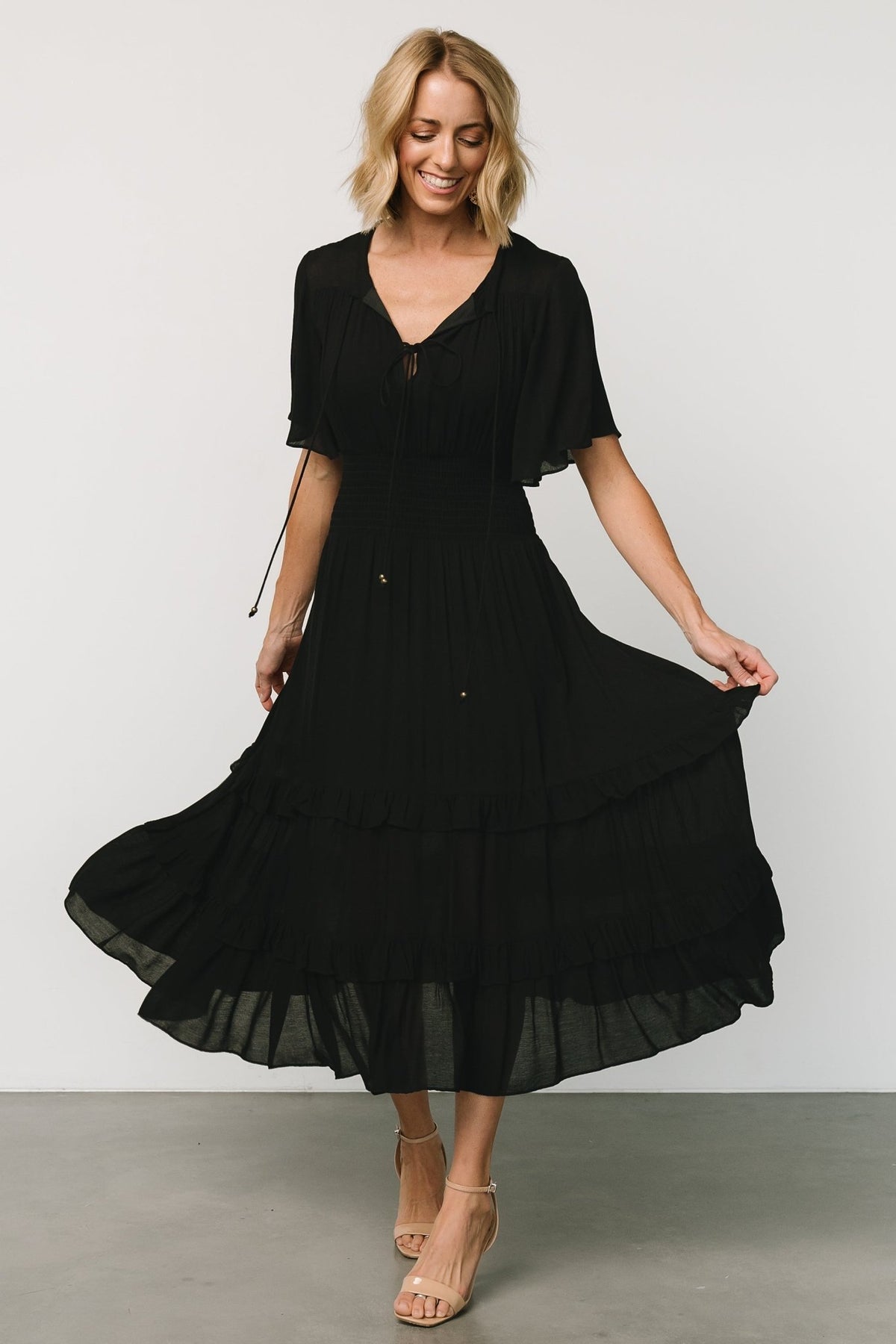 Front view of a model wearing a black boho midi dress with V-neckline, smocked waist and a fully lined midi skirt for smooth drape.