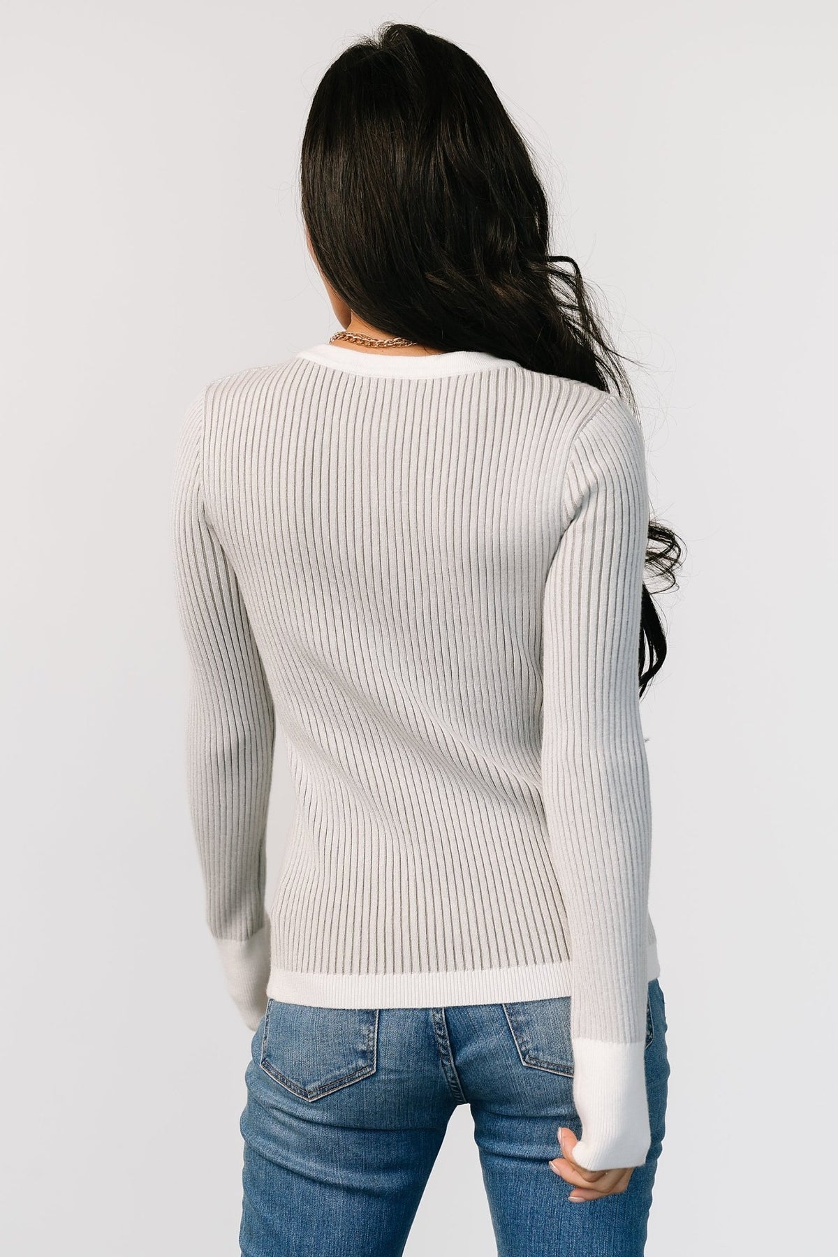 Model seated wearing Stevie ribbed sweater in gray; demonstrates relaxed fit, sleeve length, and how the sweater layers with bottoms.