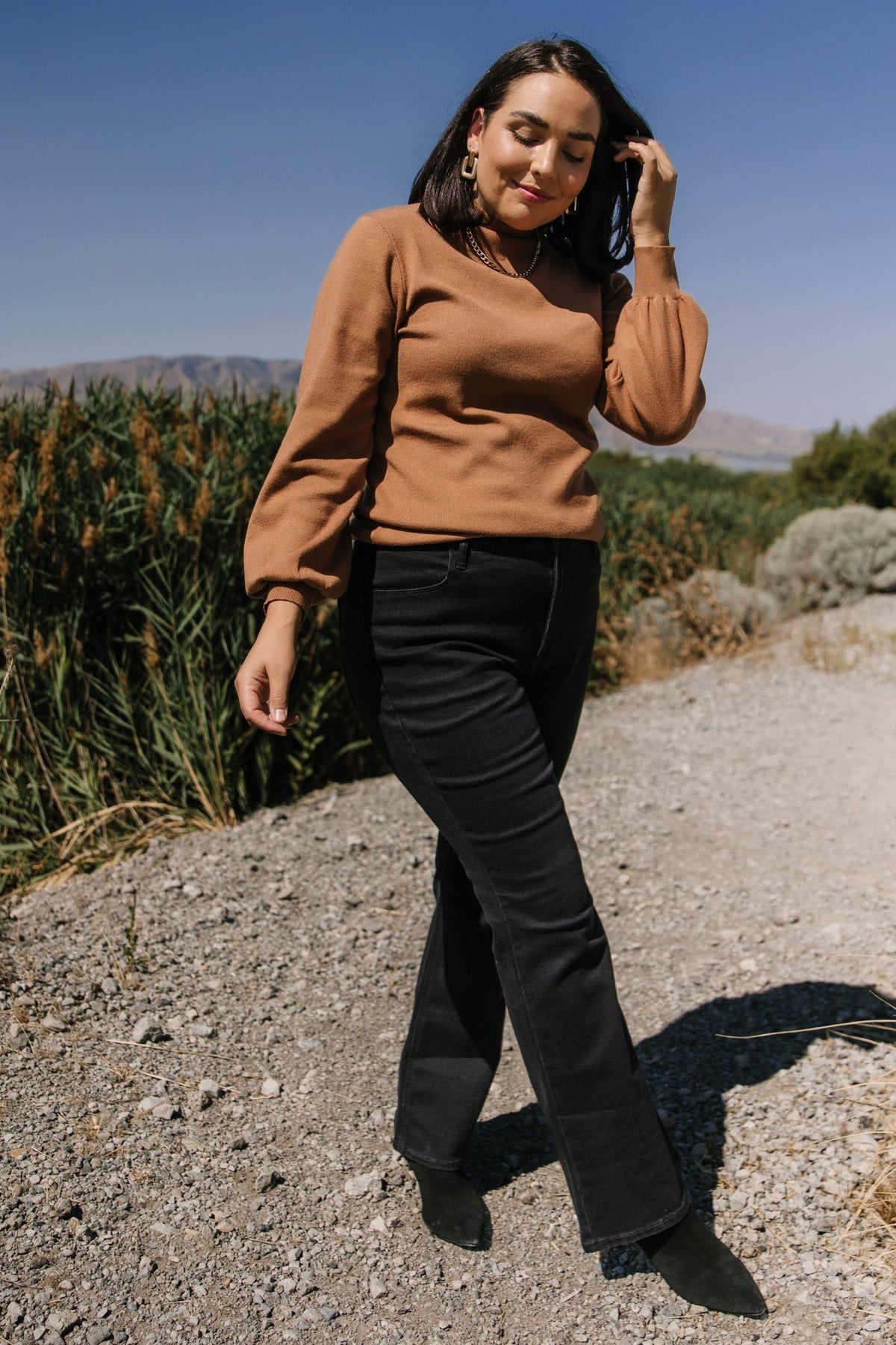 Side profile of Sutton Sweater Top in brown worn with high-waist bottoms, highlighting long bubble sleeve shape and ribbed cuff detail against a neutral background.