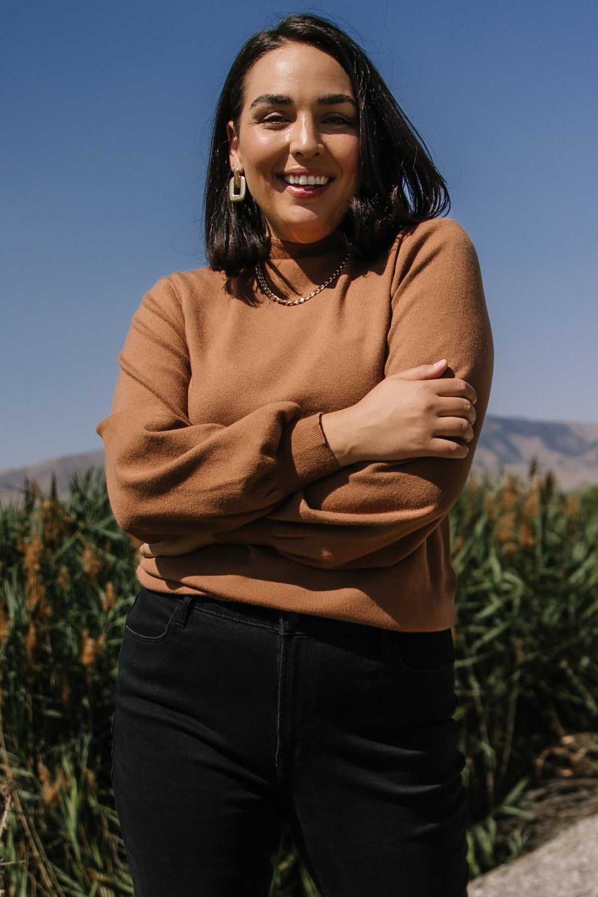 Model wearing Sutton Sweater Top in brown styled with a skirt, showing the sweater's length, relaxed silhouette and bubble sleeve proportion.
