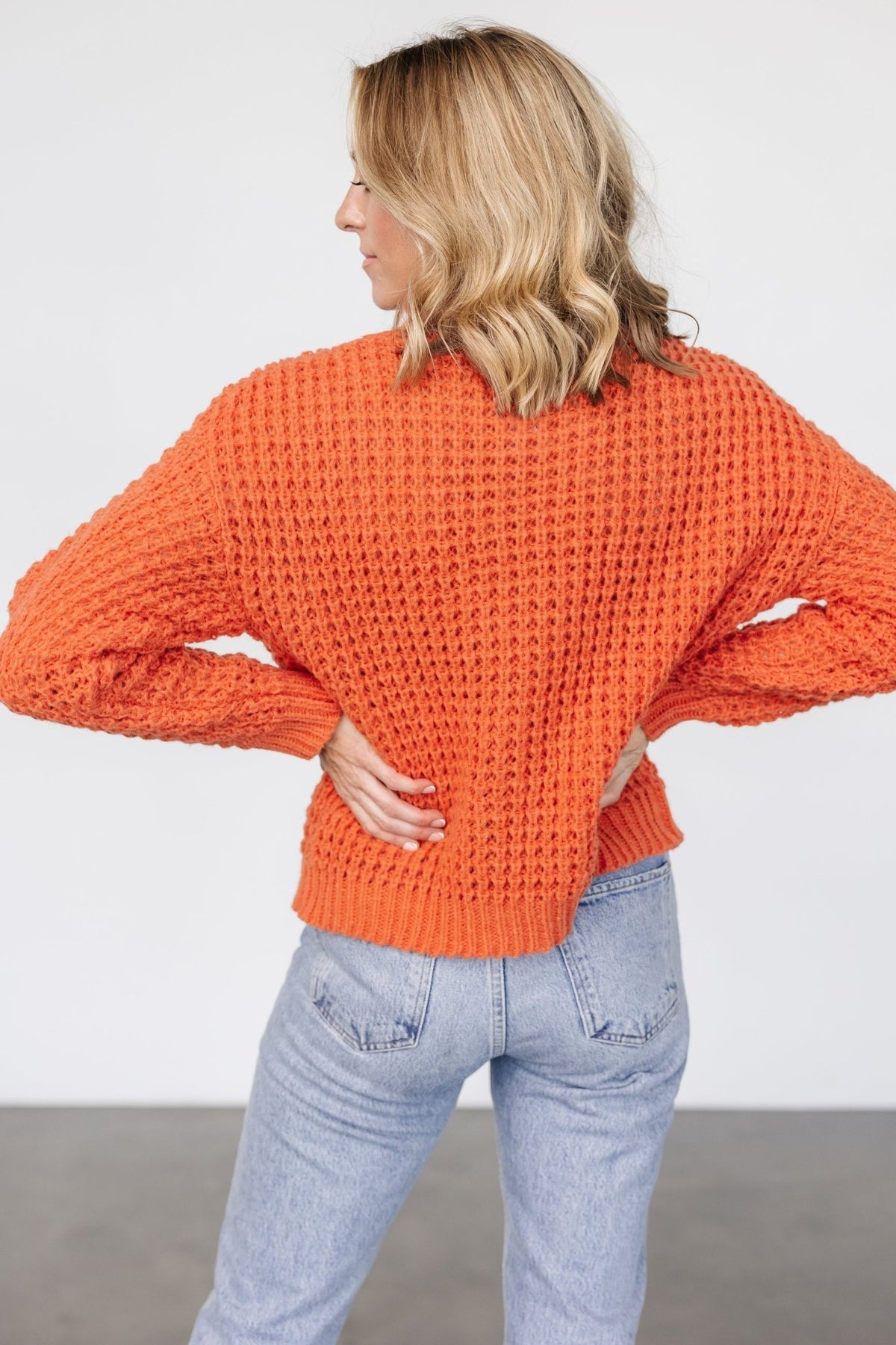 Lifestyle image of the apricot orange chunky knit sweater styled with casual bottoms, emphasizing texture, color, and the cozy rolled funnel neck for crisp weather.