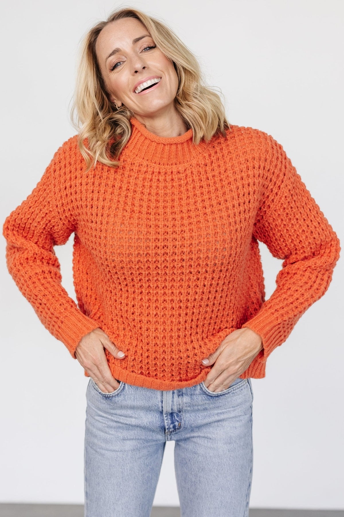 Back view of the apricot orange sweater on a model, displaying relaxed fit, ribbed hemline, and overall length for layering over jeans or skirts.