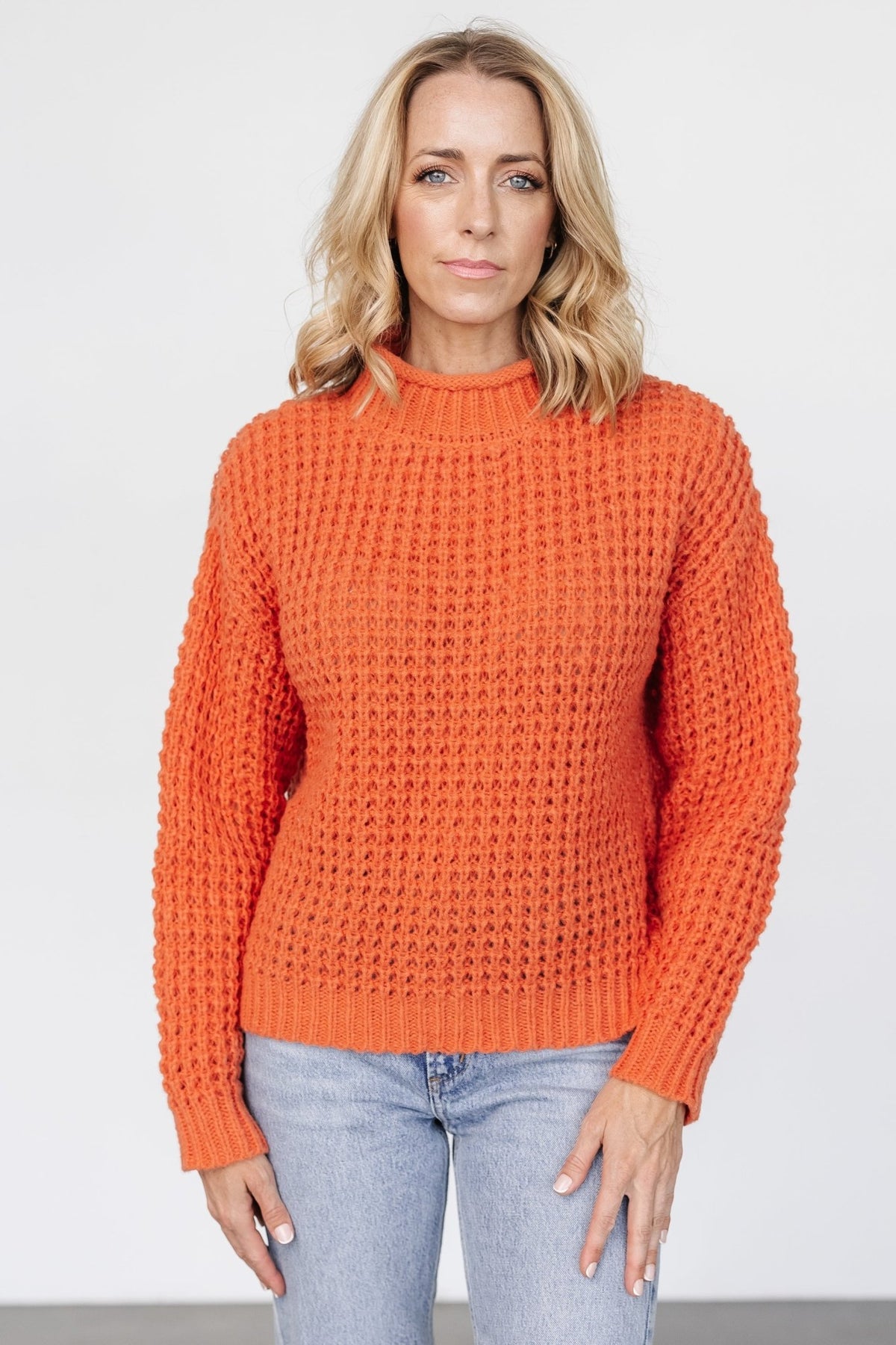Front view of an apricot orange chunky knit sweater on a model, showing rolled funnel neck and wide-ribbed cuffs in soft waffle texture (product front).