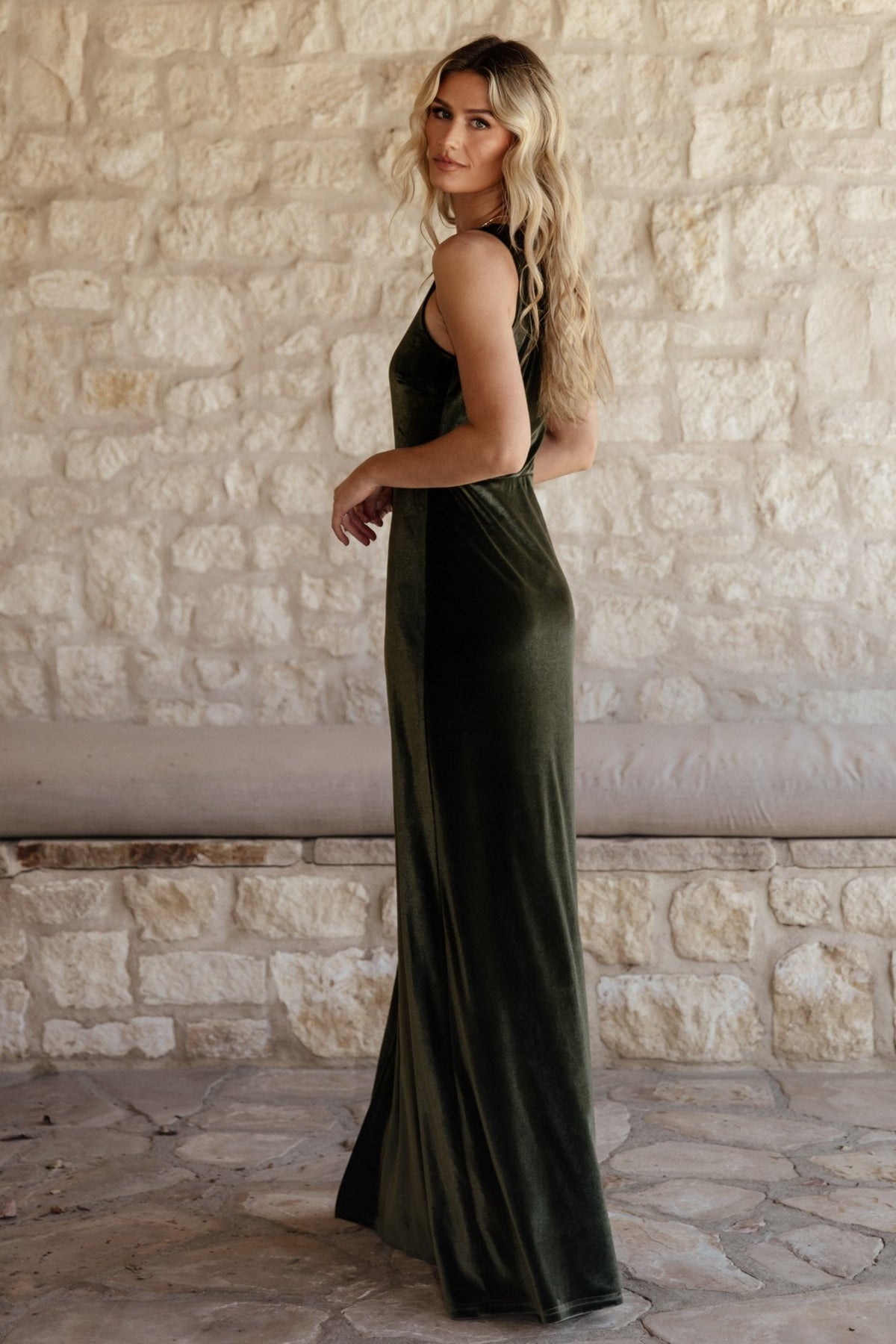Model wearing olive one-shoulder velvet maxi dress; fitted bodice, flowing skirt, and slit visible—shows natural drape and formal styling possibilities.