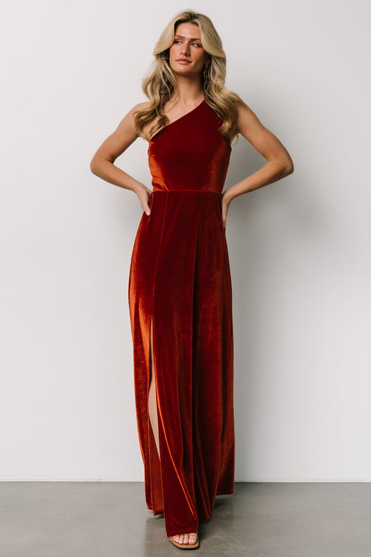 Front view of rust velvet one-shoulder maxi dress on model, fitted bodice, asymmetrical neckline and mid-thigh side slit, full-length view.