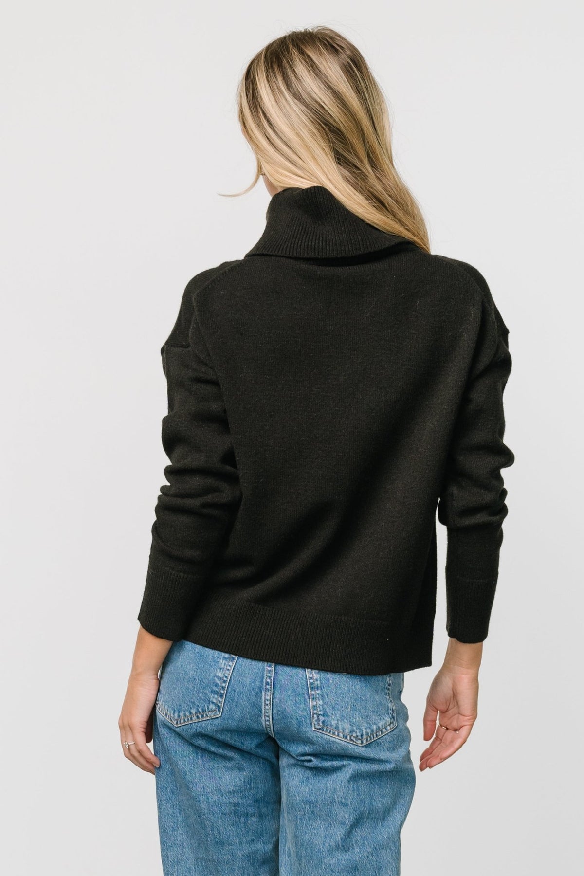 Detail shot of sleeve and cuff on black turtleneck sweater, emphasizing wide knit trim and soft blended fabric composition.