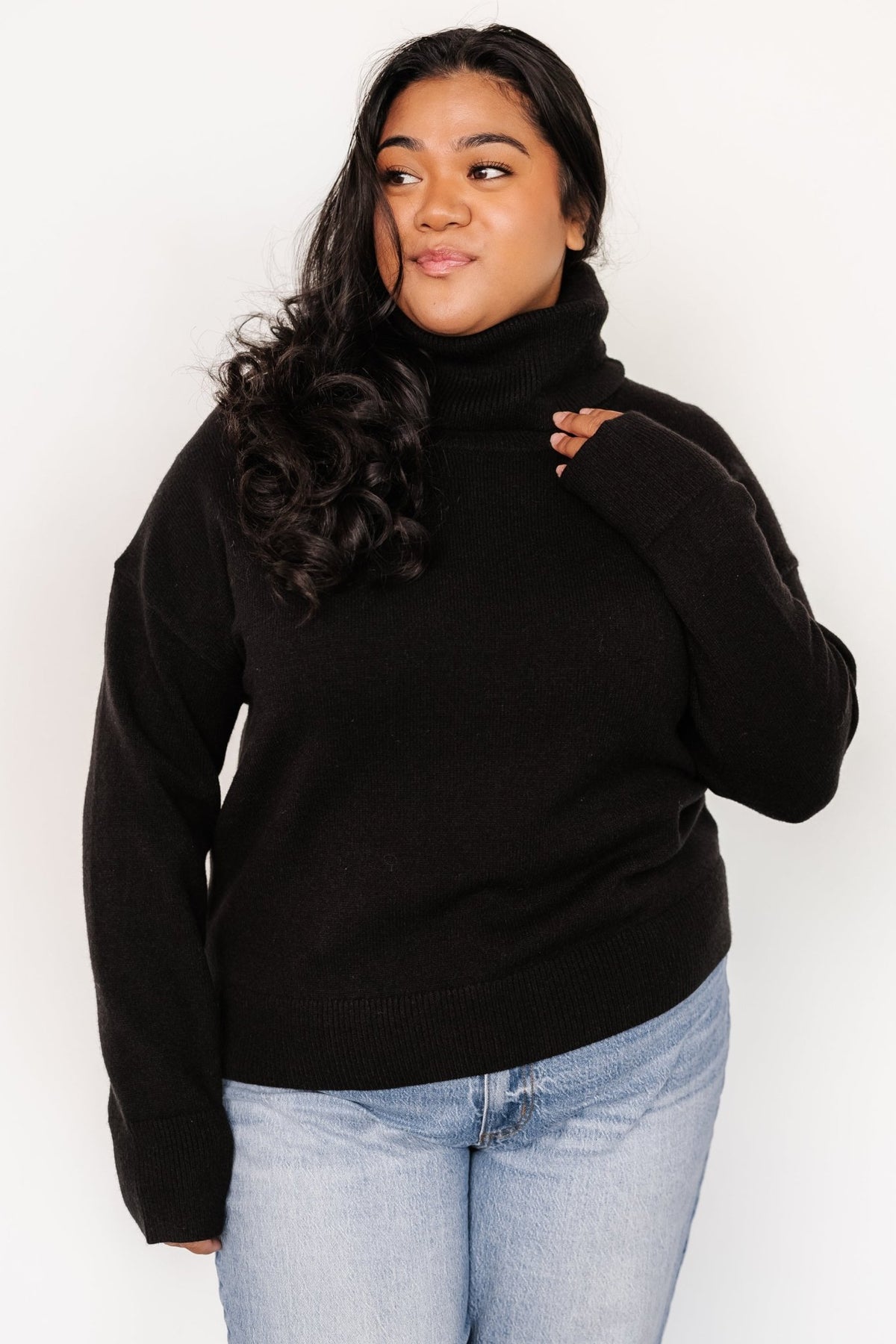 Side profile of a black cowl neck sweater highlighting the relaxed fit, dropped shoulder, and textured fine knit detail.