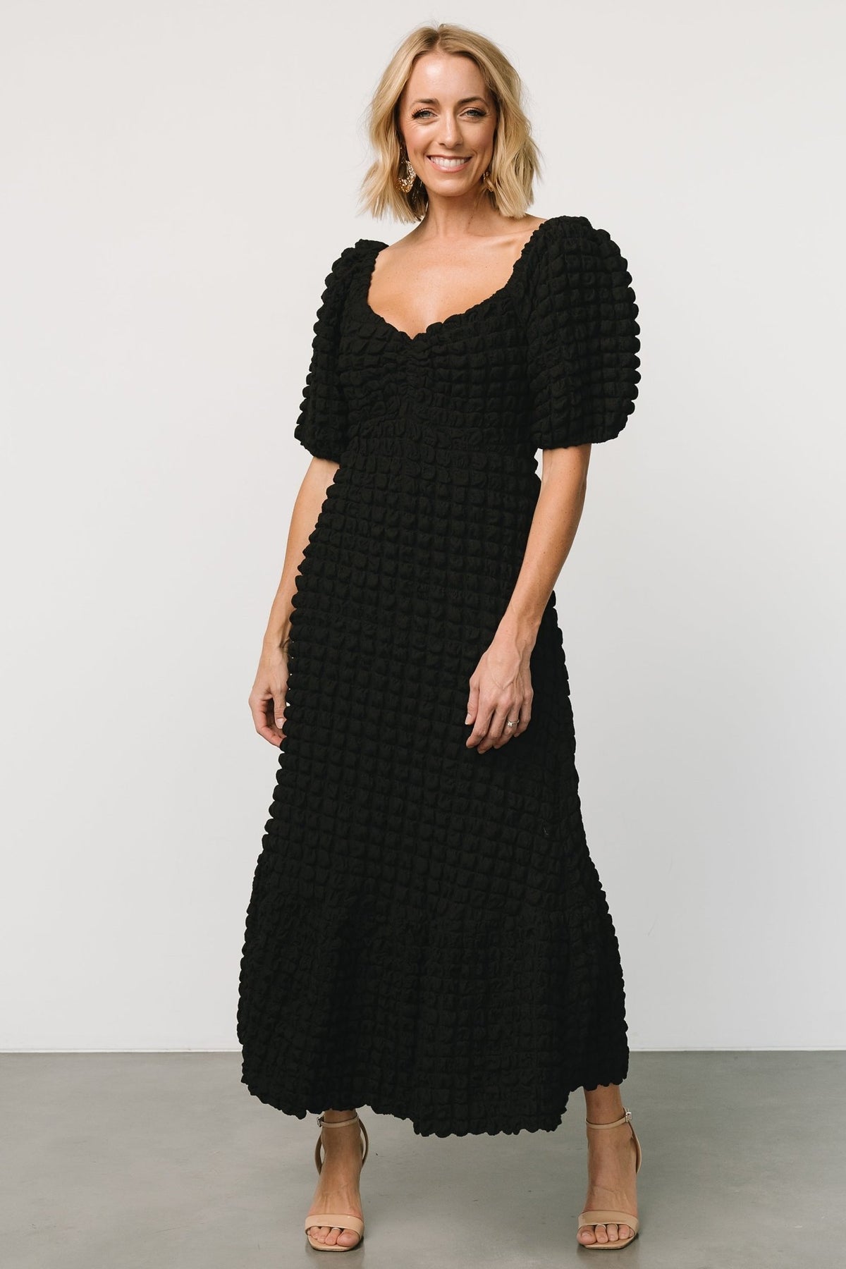 Studio image showing the skirt drape and lining to the knee on the Therese textured midi dress in black.