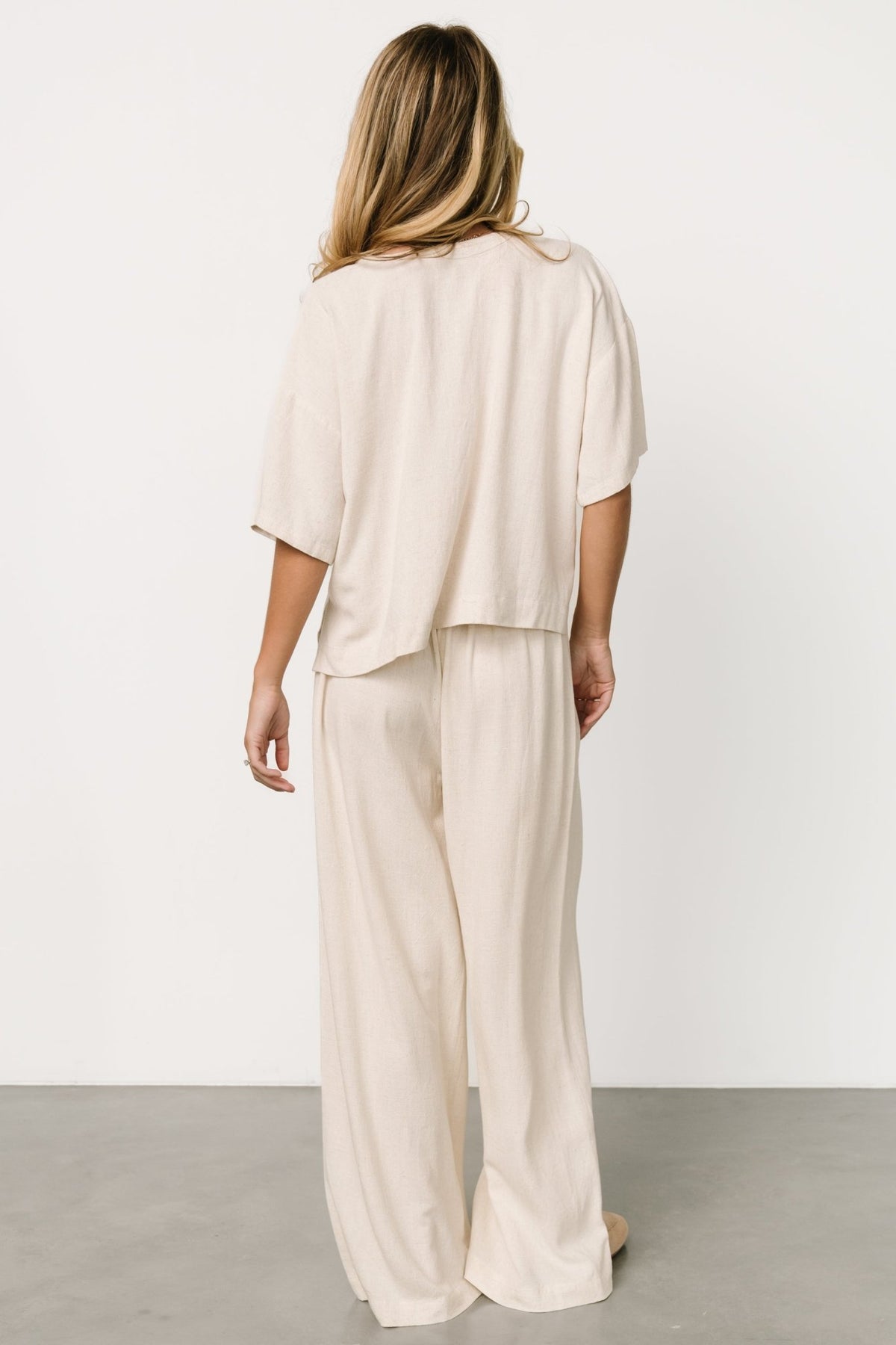 Back view of the natural two-piece set showing the relaxed silhouette and raw hem finish on the wide-leg pants.