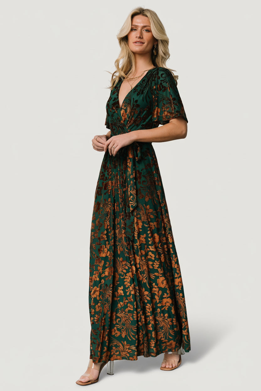 Model walking in Uma Velvet Maxi Dress in bronze and jade, showing full maxi silhouette, leg slit, and natural fabric drape.