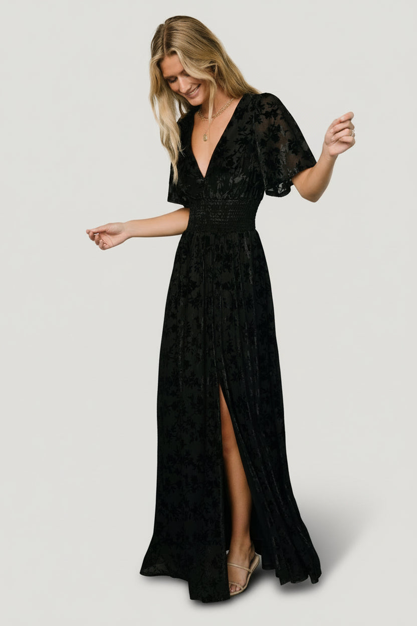 Side view of black Veronica Velvet Maxi Dress on model showing left leg slit, movement in skirt, and unlined short sleeves.