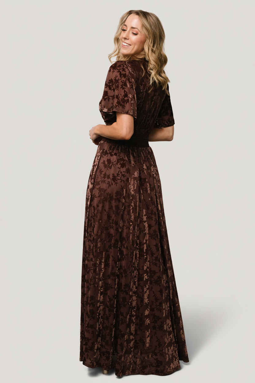 Side view of Veronica Velvet Maxi Dress in espresso on model, showing smocked stretch waist and the flowy short sleeves in motion.