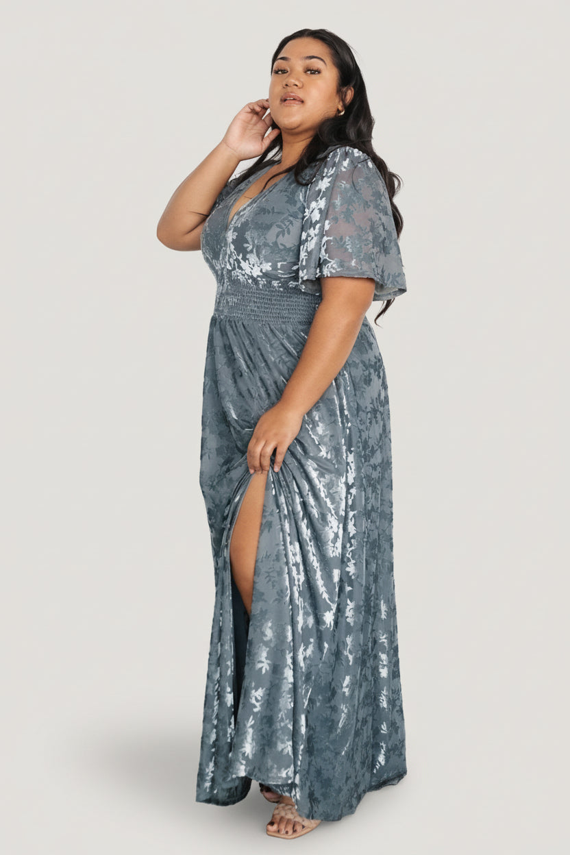 Styled product shot of Veronica velvet maxi in slate blue paired with neutral heels to show overall length, silhouette, and smocked waist detail.