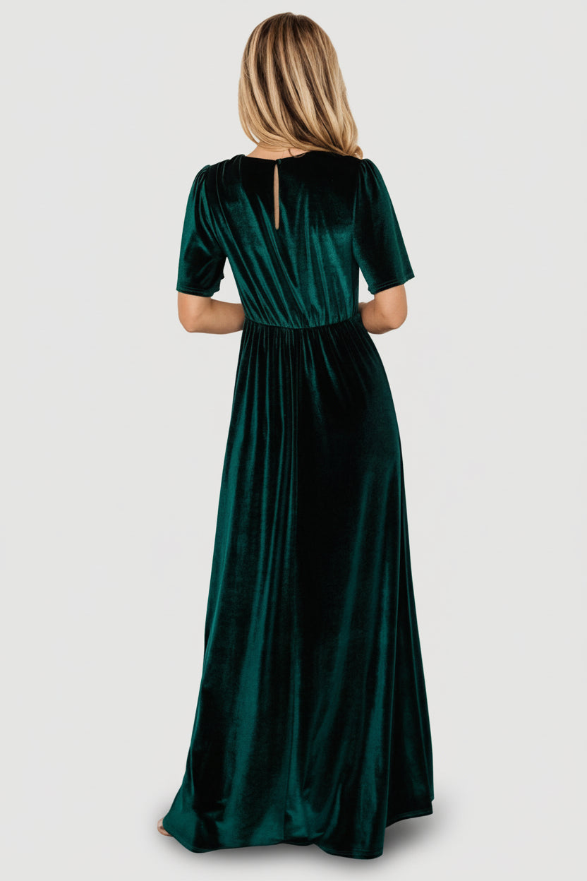 Styled shot of the emerald Vivian velvet maxi dress paired with heels, showing full silhouette, deep V-neck, and gown-length hem.